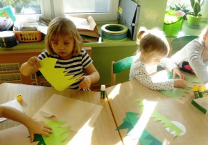 Dzieci siedzą przy stolikach i wykonują grzybki z kolorowych kół